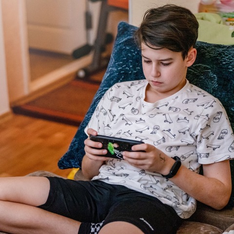 Έφηβος κρατά το κινητό του ενώ κάθεται σε μαξιλάρια