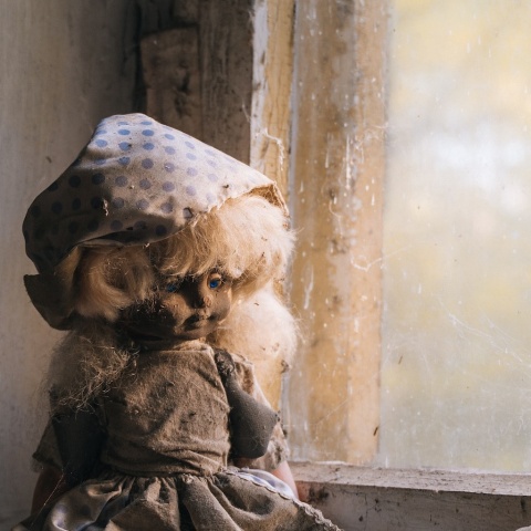 Λερωμένη και ταλαιπωρημένη κούκλα σε σκονισμένο παράθυρο