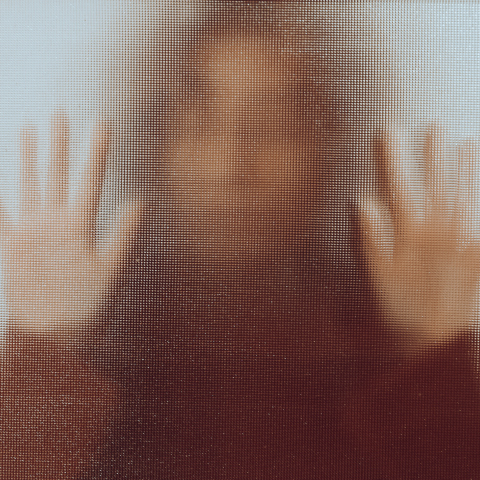 Γυναίκα πίσω από ημιδιάφανο τζάμι με κολλημένα τα χέρια της στην επιφάνεια σε στάση που παραπέμπει σε φόβο και απόγνωση