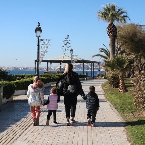 Μητέρα με τα τρία της παιδιά απολαμβάνουν τον καλό καιρό και τον ήλιο περπατώντας δίπλα στη θάλασσα