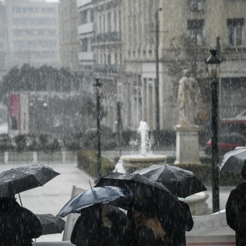 Πολίτες με ομπρέλα περπατούν υπό καταρρακτώδη βροχή στο κέντρο της Αθήνας