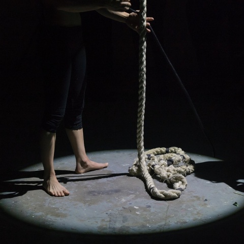 Άτομο με γυμνά πόδια κρατά χοντρό σκοινί σε σκοτεινό δωμάτιο - Εικόνα που παραπέμπει σε αυτοκτονία δι' απαγχονισμού