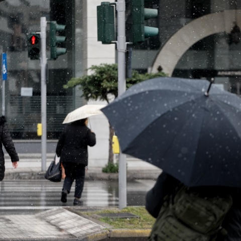 Πολίτες με ομπρέλα κατά τη διάρκεια ελαφράς χιονόπτωσης στο κέντρο της Αθήνας