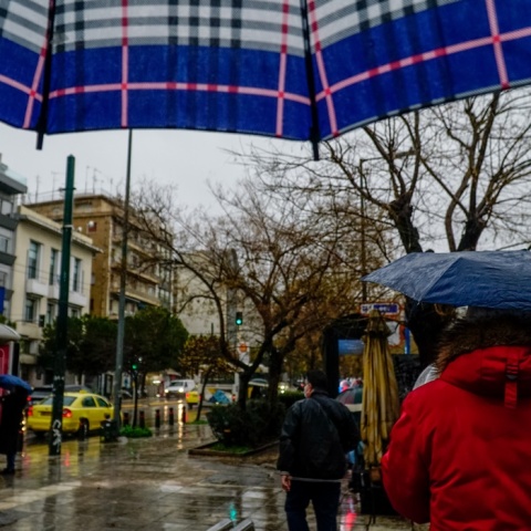 Πολίτες με ομπρέλα προστατεύονται από τη βροχή στο κέντρο της Αθήνας