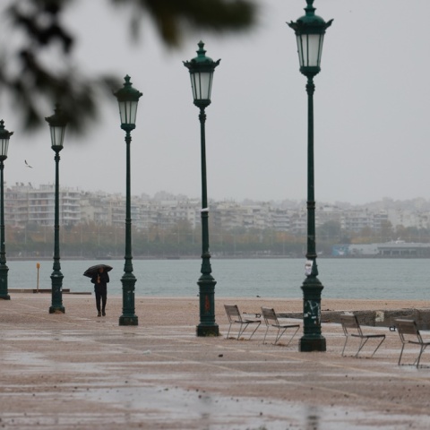 Πολίτης με ομπρέλα περπατά στη βροχερή παραλία της Θεσσαλονίκης