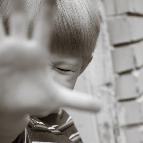 Παιδί προτάσσει το χέρι του και σφίγγει τα μάτια του υπό την απειλή φόβου