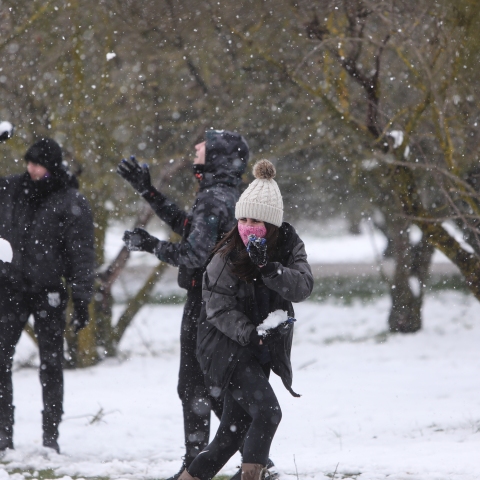 Νεαρά άτομα παίζουνε με το χιόνι, φορώντας ζεστά ρούχα