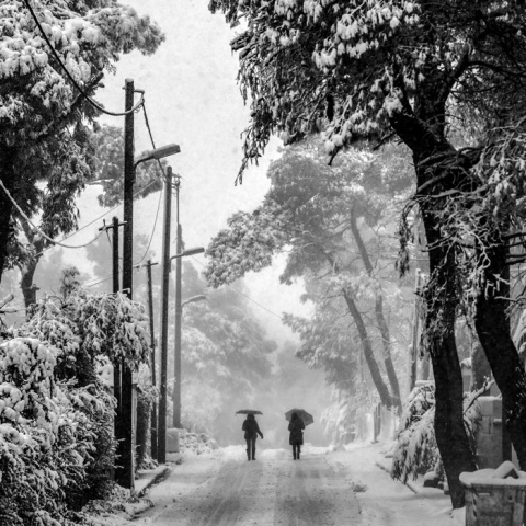Χιονισμένο τοπίο και δύο πολίτες περπατούν κρατώντας την ομπρέλα τους