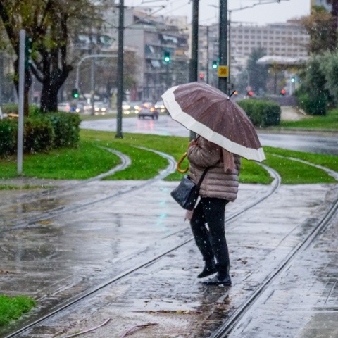 Γυναίκα με ομπρέλα περπατά σε βρεγμένο δρόμο 