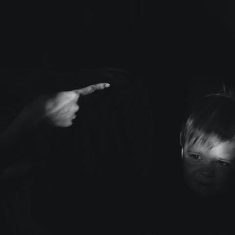 Γυναίκα τείνει το χέρι κατά παιδιού σε σκοτεινό δωμάτιο - Εικόνα που παραπέμπει σε κακοποιητική συμπεριφορά