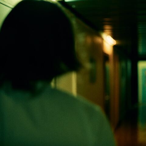 Γυναίκα γυρισμένη πλάτη σε σκοτεινό διάδρομο - Εικόνα που παραπέμπει σε κακοποίηση και μυστήριο