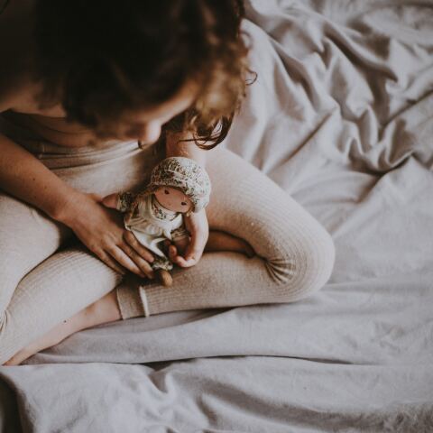 Παιδί κάθεται οκλαδόν σε κρεβάτι και κρατά στα χέρια του κούκλα