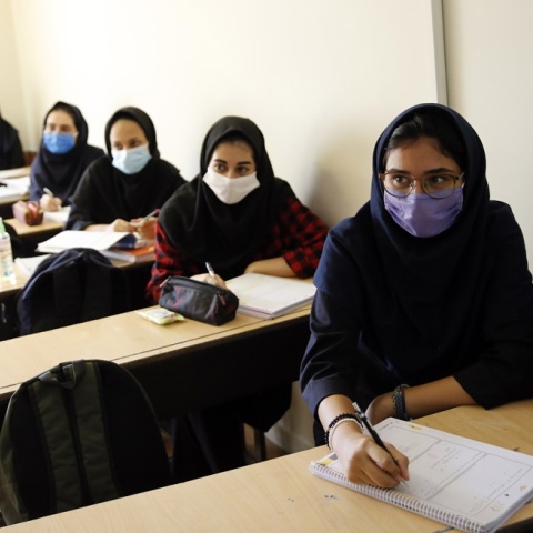 Μαθήτριες σε σχολείο στο Ιράν κάθονται στα έδρανα έχοντας ανοίξει τα τετράδια τους και φορώντας τις μάσκες τους