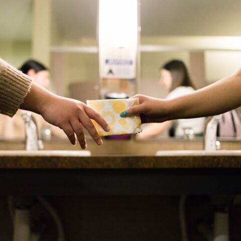 Κοπέλα δίνει σε άλλη κοπέλα σερβιέτα μέσα σε τουαλέτα