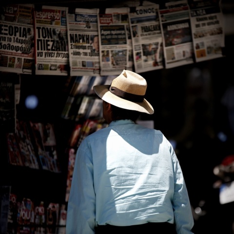 Εφημερίδες κρεμασμένες σε περίπτερο και άνδρας με καπέλο να διαβάζει τα πρωτοσέλιδα