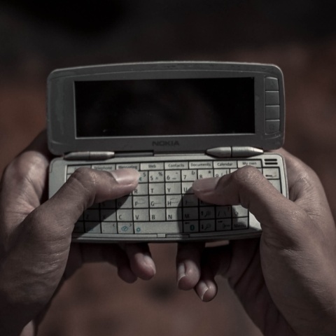 Γυναίκα κρατά στα χέρια της ένα παλιό κινητό και πληκτρολογεί