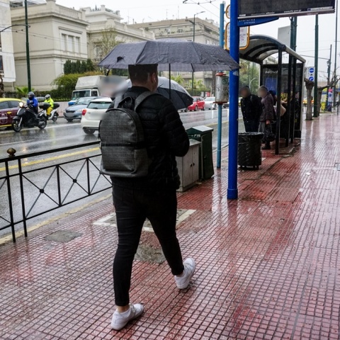 Νεαρός με ομπρέλα περπατά σε δρόμο της Αθήνας ενώ βρέχει