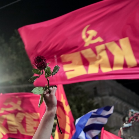 Σημαίες του ΚΚΕ και ένα χέρι που προτάσσει ένα κόκκινο λουλούδι