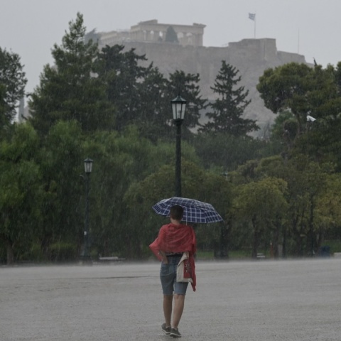 Γυναίκα με ομπρέλα περπατά σε δρόμο της Αθήνας