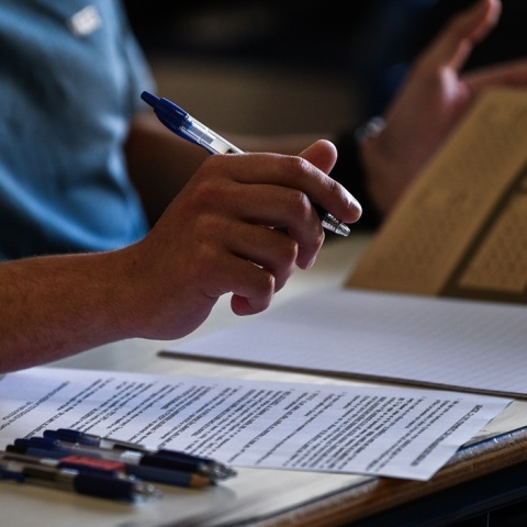 Το τετράδιο απαντήσεων για τα θέματα των Νέων Ελληνικών στα οποία εξετάστηκαν τα ΕΠΑΛ - Οι κόλλες με τα θέματα και στιλό πάνω στο θρανίο - Διακρίνεται το χέρι υποψηφίου