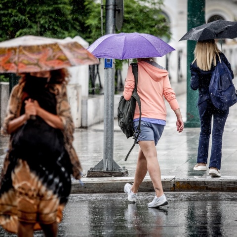 Γυναίκες με ομπρέλες στο κέντρο της Αθήνας προστατεύονται από αστάθεια του καιρού που εκδηλώνεται με καταιγίδες τις μεσημεριανές ώρες