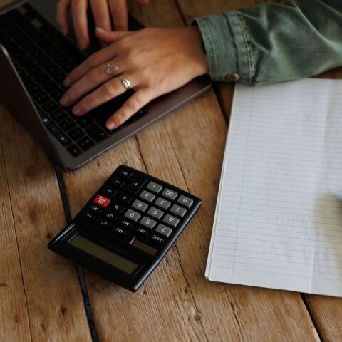 Άτομο υπολογίζει τα οικονομικά του σε κομπιουτεράκι, υπολογιστή και χαρτί