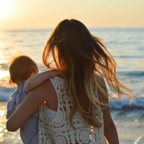 Μητέρα με το παιδί στην αγκαλιά της στην ακροθαλασσιά - Τα μαλλιά της ανεμίζουν