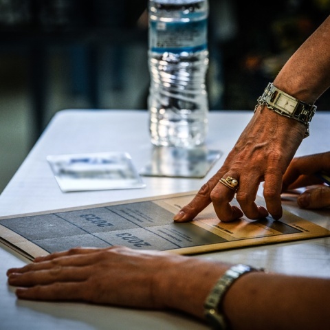 Χέρι επιτηρητή και υποψήφιας των Πανελληνίων 2023 πάνω από το τετράδιο απαντήσεων