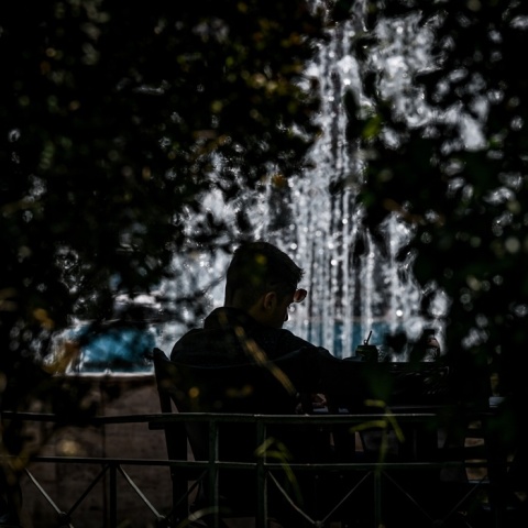 Πολίτης κάθεται σε καφέ κοντά σε σιντριβάνι και υπό τον ίσκιο φυτών