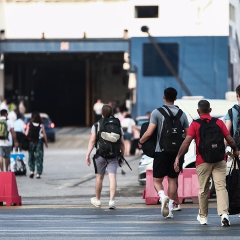 Ταξιδιώτες με τις βαλίτσες τους ετοιμάζονται για επιβίβαση σε πλοίο στο λιμάνι του Πειραιά