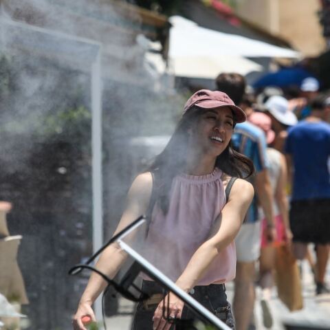 Κοπέλα περνά μπροστά από ανεμιστήρα που ψεκάζει νερό