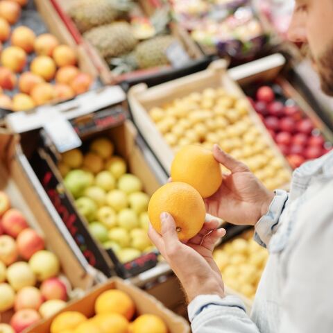 Άνδρας κρατά πορτοκάλια μπροστά από τον τομέα με φρούτα και λαχανικά σε σούπερ μάρκετ