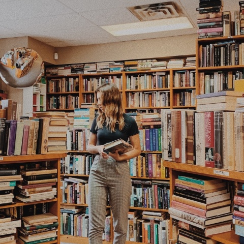 Νεαρή γυναίκα σε βιβλιοπωλείο εξετάζει προσεκτικά τα βιβλία που επιθυμεί να αγοράσει