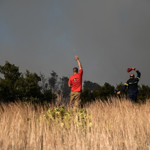 Πυροσβέστης και εθελοντής μακριά από το πύρινο μέτωπο επιτηρούν φωτιά που καίει χαμηλή βλάστηση