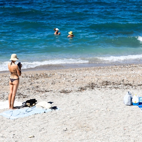 Γυναίκα σε παραλία όρθια κοντά στην απλωμένη πετσέτα της - παραλία με λίγο κυματάκι