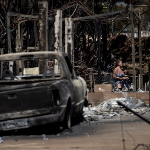 Καμένα αυτοκίνητα και σπίτια από τις φονικές πυρκαγιές στο Μάουι της Χαβάης και γυναίκα στο σημείο