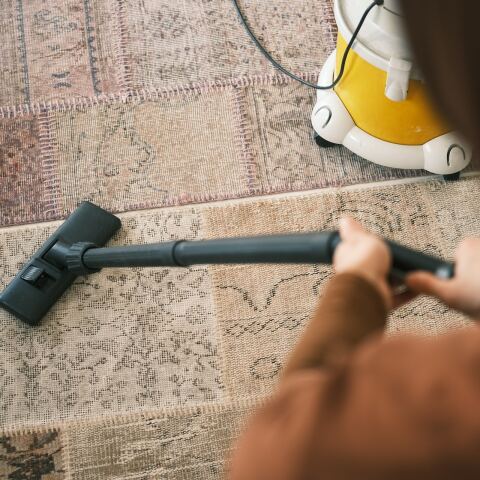 Άτομο κρατά ηλεκτρική σκούπα και καθαρίζει χαλί