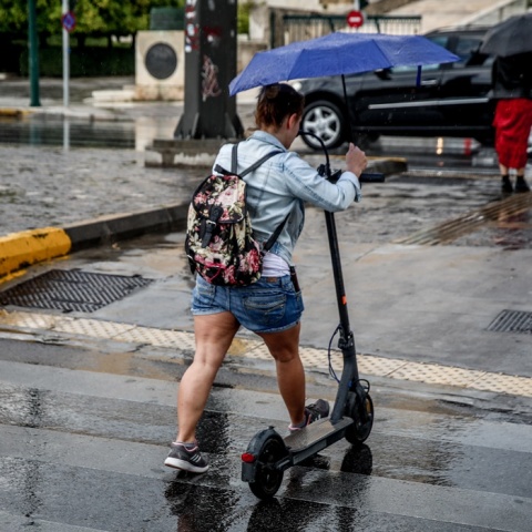 Γυναίκα με πατίνι κρατά ομπρέλα για να προστατευτεί από τη βροχή