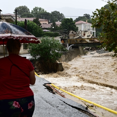 Γυναίκα περπατά με την ομπρέλα της δίπλα σε ποτάμι με ορμητικά νερά