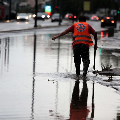 Πλημμυρισμένο σημείο της οδού Πειραιώς και άτομο που επιχειρεί να ανοίξει φρεάτια