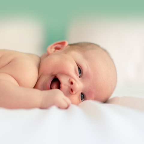 Μωρό που χαμογελά ξαπλωμένο σε λευκό σεντονάκι