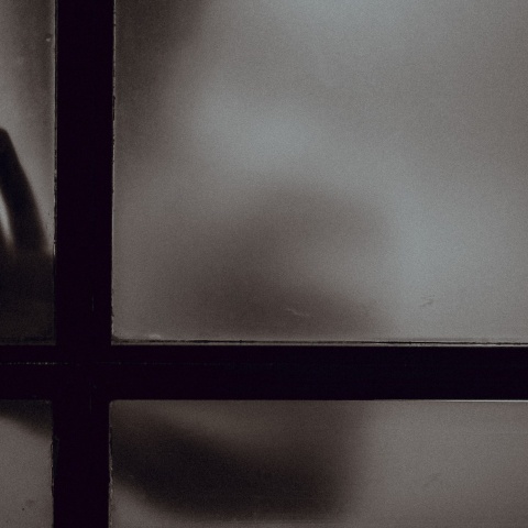 Σκοτεινή φωτογραφία με χέρι ατόμου πίσω από κλειστή πόρτα