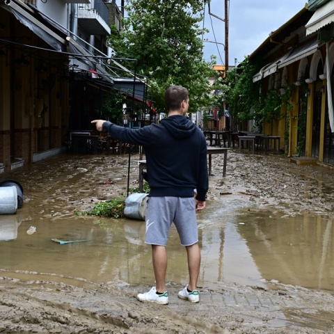 Άνδρας γυρισμένος πλάτη στον φωτογραφικό φακό περπατά σε λάσπες σε δρόμο στο κέντρο της πόλης του Βόλου μετά την κακοκαιρία Daniel