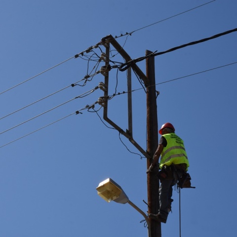 Άνδρας πραγματοποιεί εργασίες σκαρφαλωμένος σε κολώνα της ΔΕΗ - Φορά ανακλαστικό και προστατευτικό κράνος