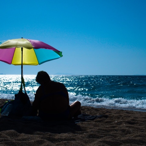 Άνδρας καθισμένος κάτω από πολύχρωμη ομπρέλα θαλάσσης στην ακροθαλασσιά