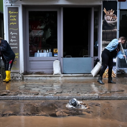 Γυναίκες με γαλότσες και σκούπες ανά χείρας απομακρύνουν από κατάστημα και πεζοδρόμια τα λασπόνερα