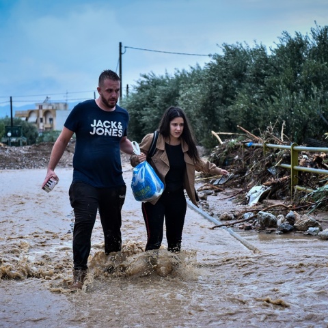 Γυναίκα και άνδρας βοηθούν ο ένας τον άλλο να περπατήσουν σε πλημμυρισμένο δρόμο στην Αγριά της Μαγνησίας