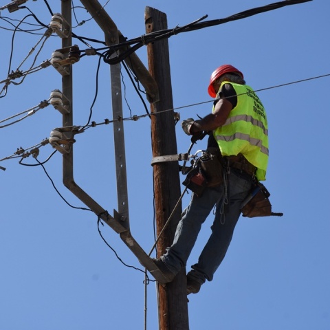 Τεχνίτης σκαρφαλωμένος σε κολώνα της ΔΕΗ φορά τα προστατευτικά ρούχα