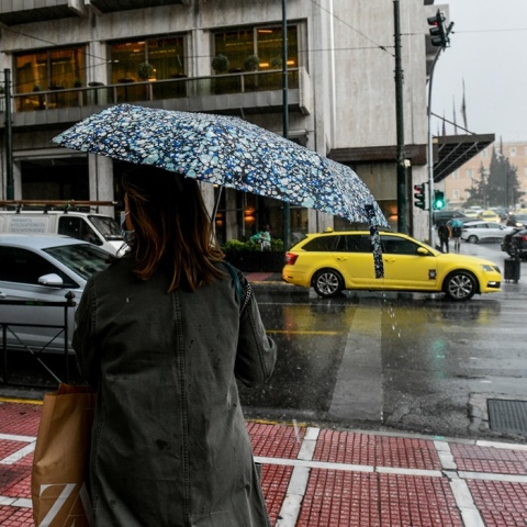 Γυναίκα με ομπρέλα σε δρόμο της Αθήνας περιμένει το φανάρι για να διασχίσει δρόμο