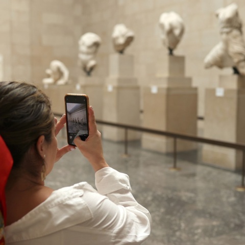 Τεκμήρια στο Βρετανικό Μουσείο και γυναίκα στα αριστερά της οθόνης που με το κινητό της τα φωτογραφίζει